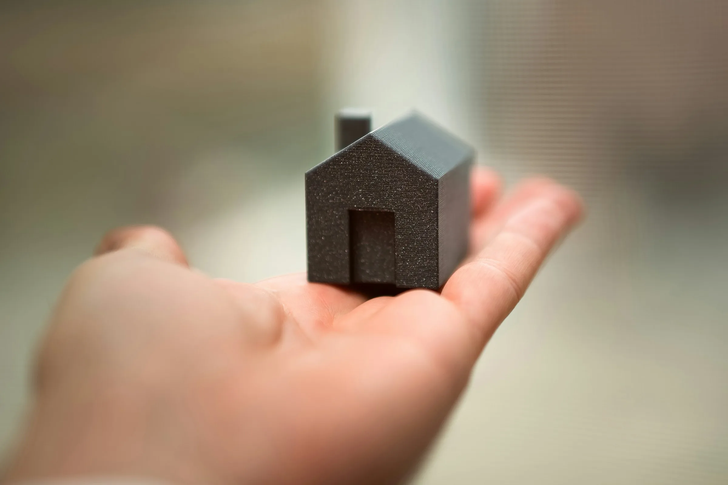 A hand holding a small dark model house in its open palm
