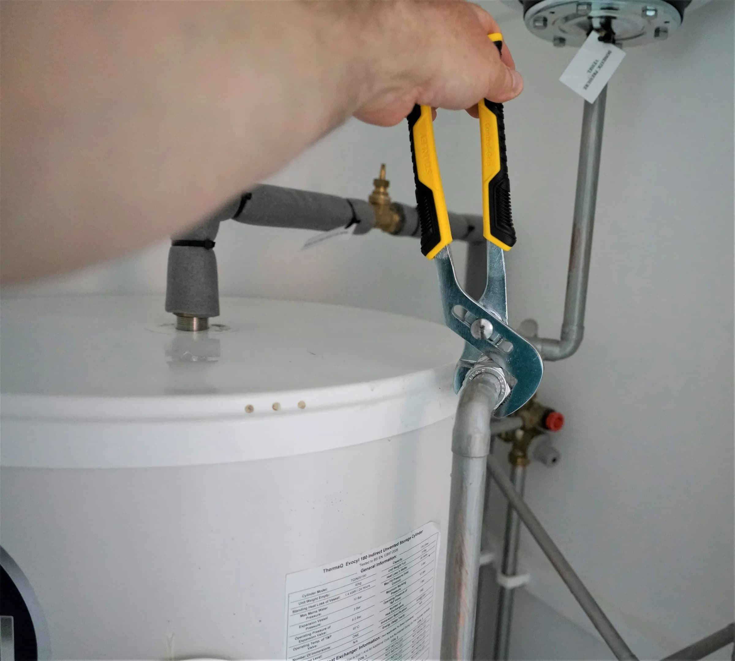 A hand using a yellow and grey wrench on a pipe joint beside a white water heater