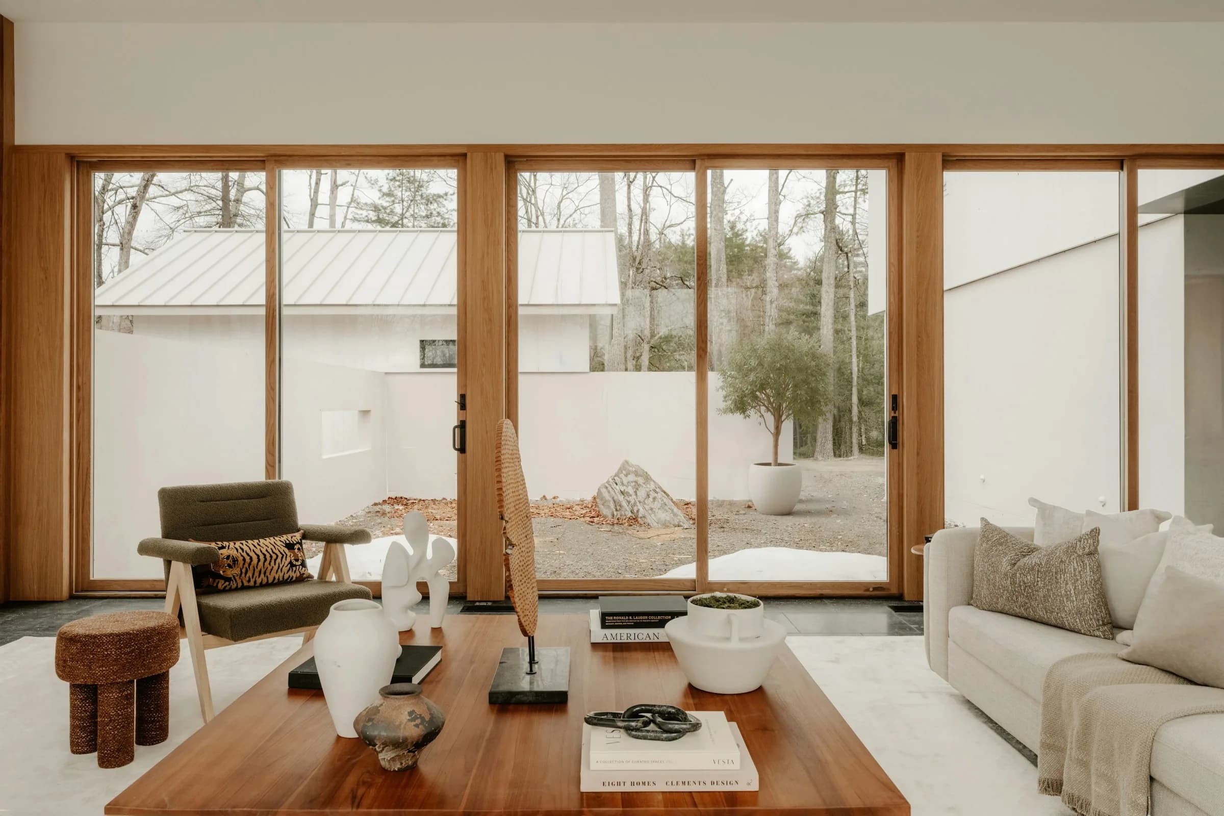 A bright, staged living room with a wooden coffee table, a cream sofa and floor-to-ceiling glass doors onto a garden