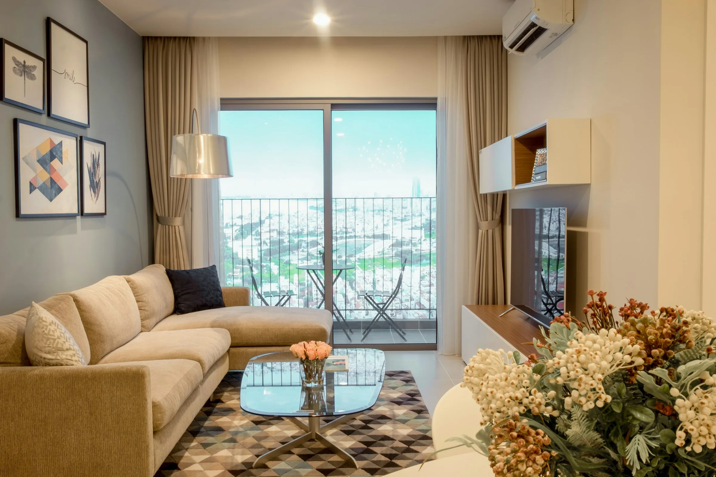 A bright living room with a mustard sofa, a glass coffee table and a balcony view