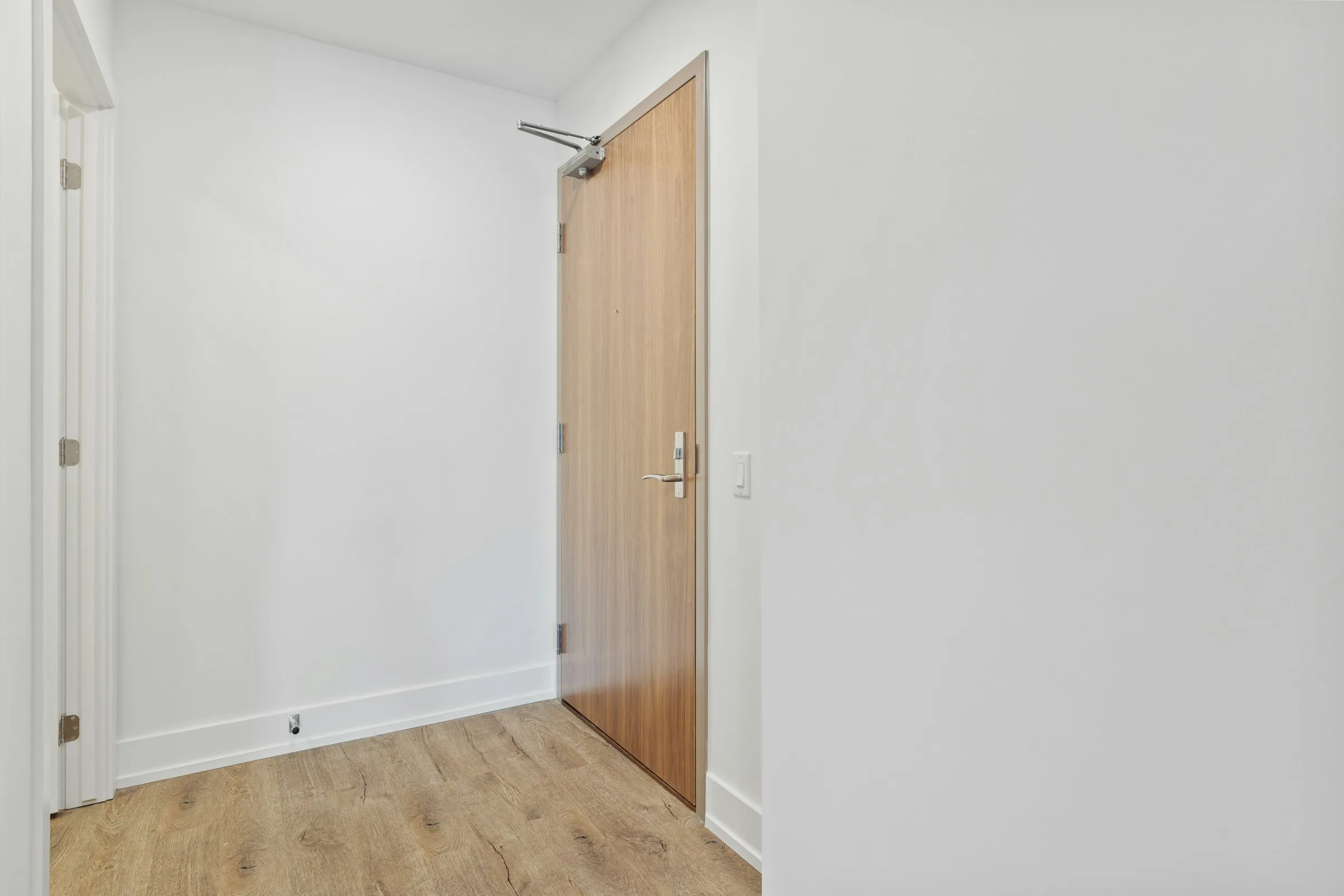 A bright empty flat with white walls, a wooden floor and a wooden interior door