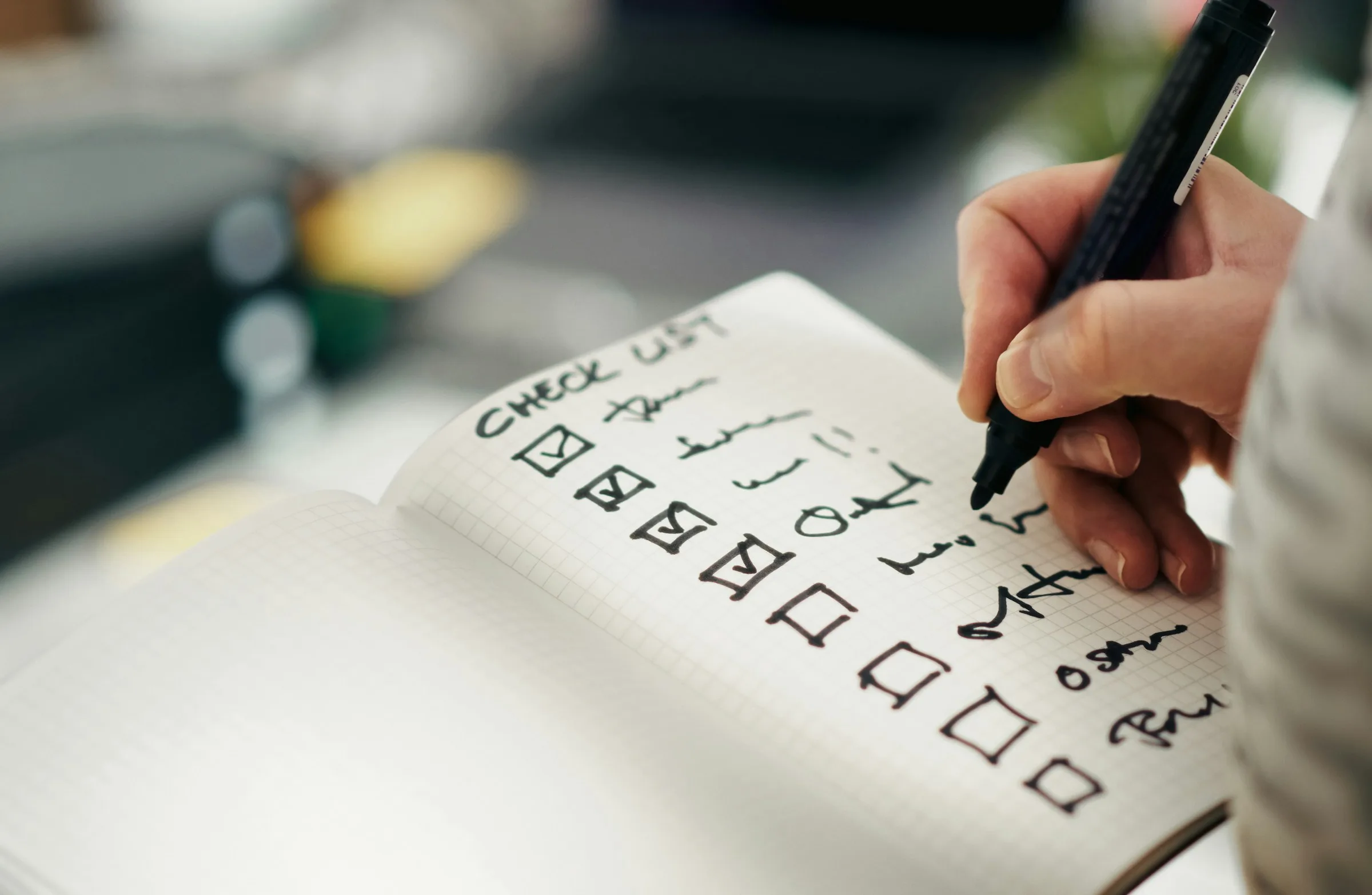 A hand ticking items off a handwritten checklist in a notebook
