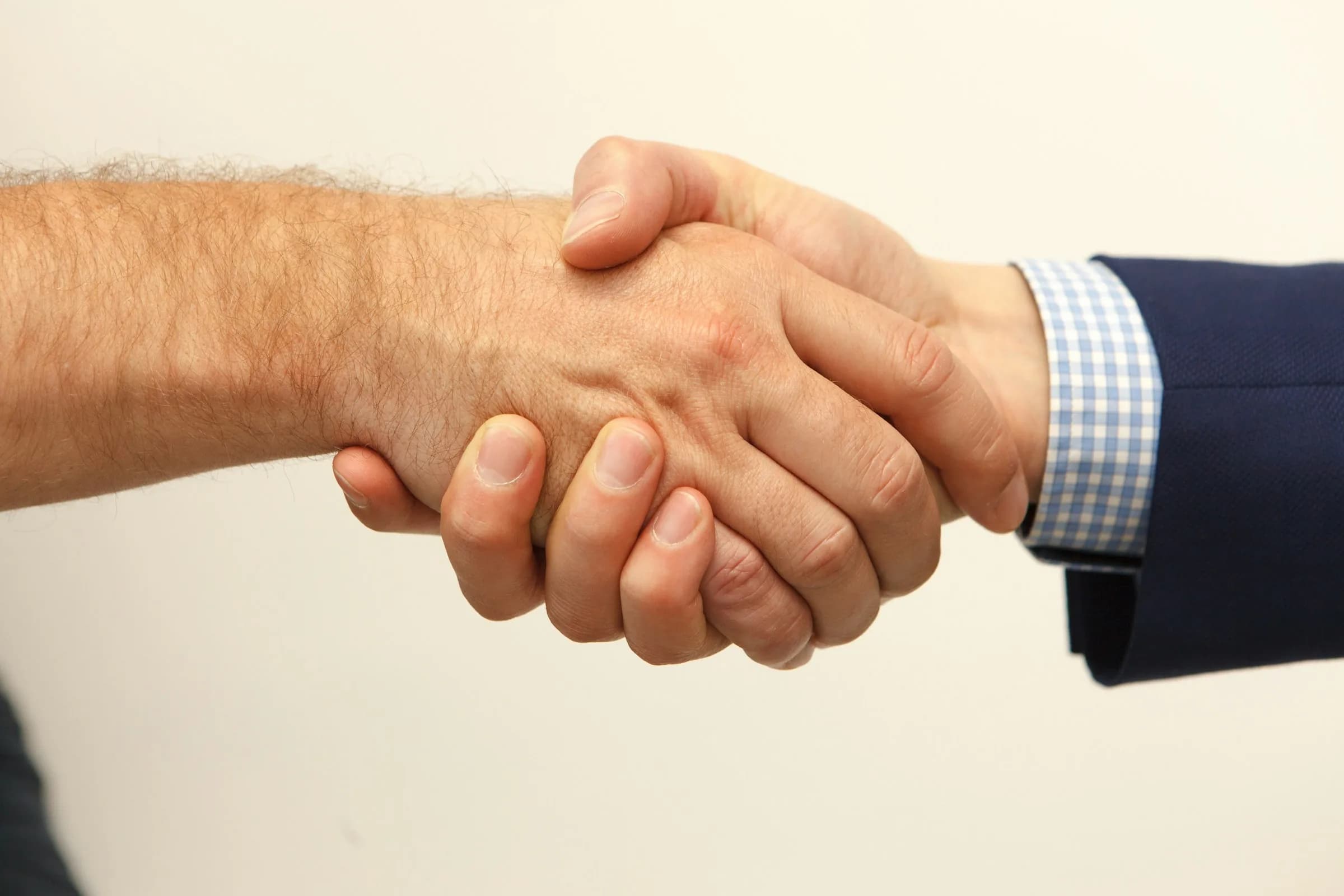 Two people shaking hands, one wearing a navy jacket over a checked shirt, against a plain pale background