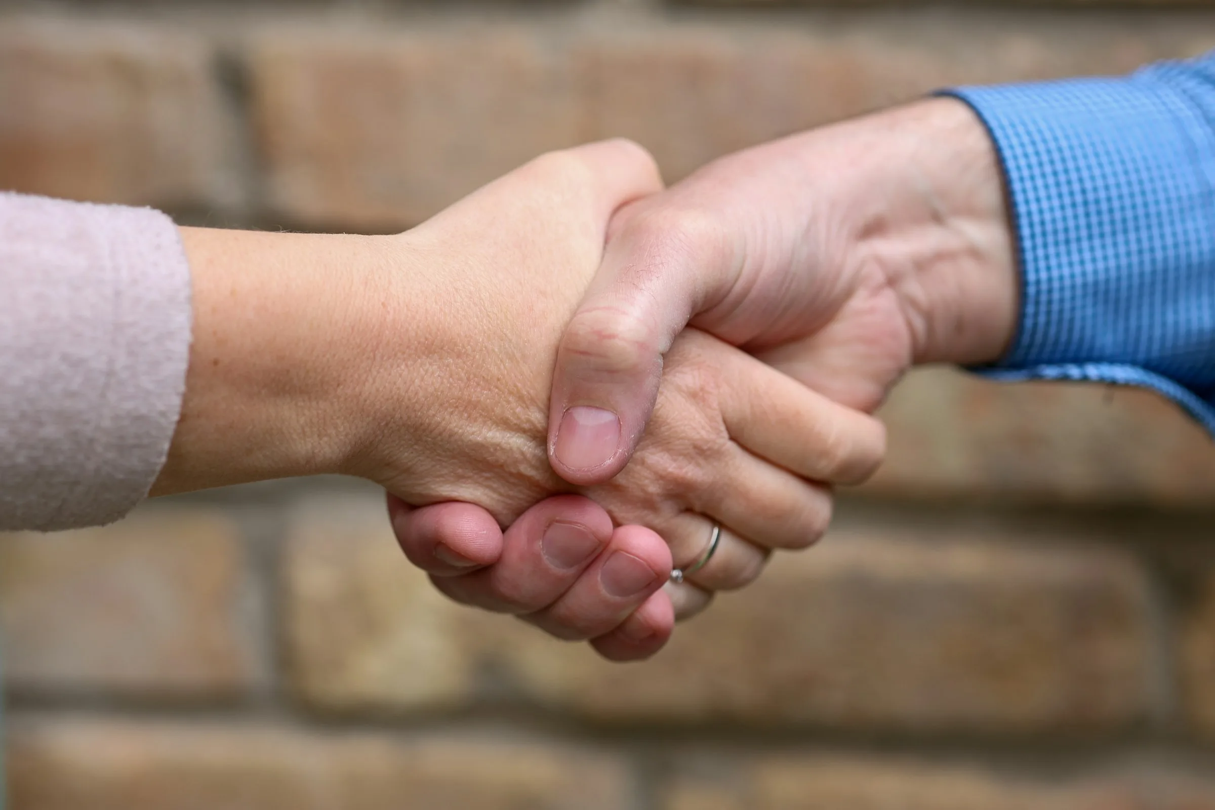 Two people shaking hands in front of a brick wall