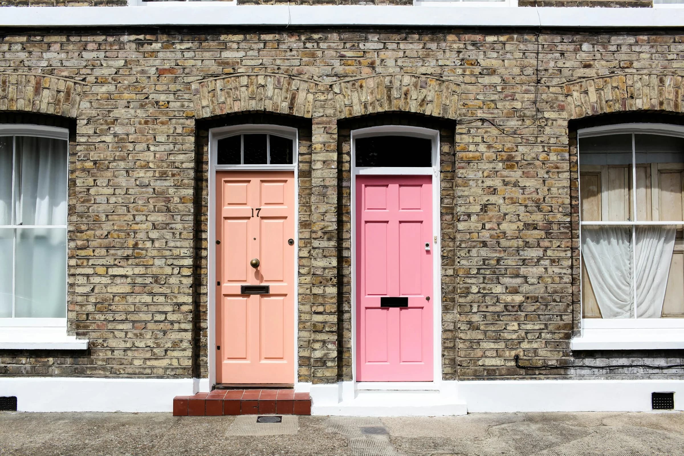 Two front doors, one peach and one pink, side by side in a terrace of pale brick houses.