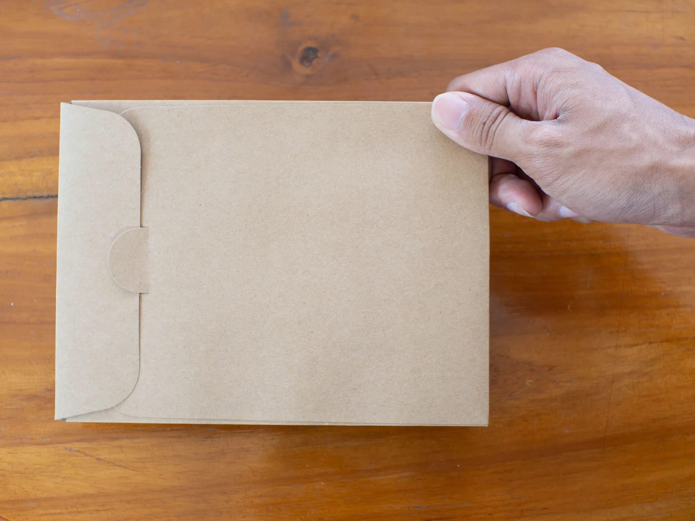 A hand resting on a plain brown envelope on a wooden table.