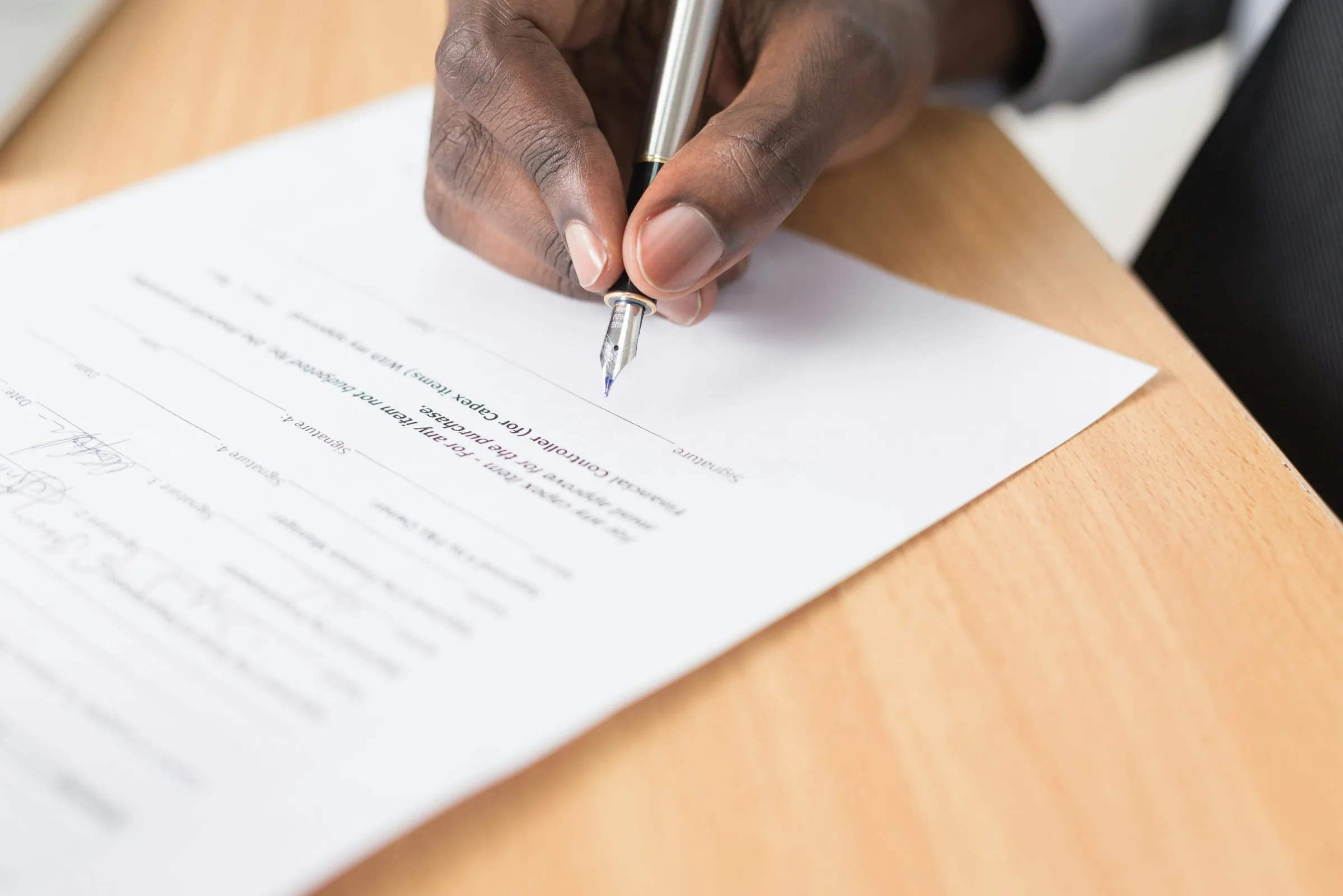 A hand signing a document on a wooden desk with a pen