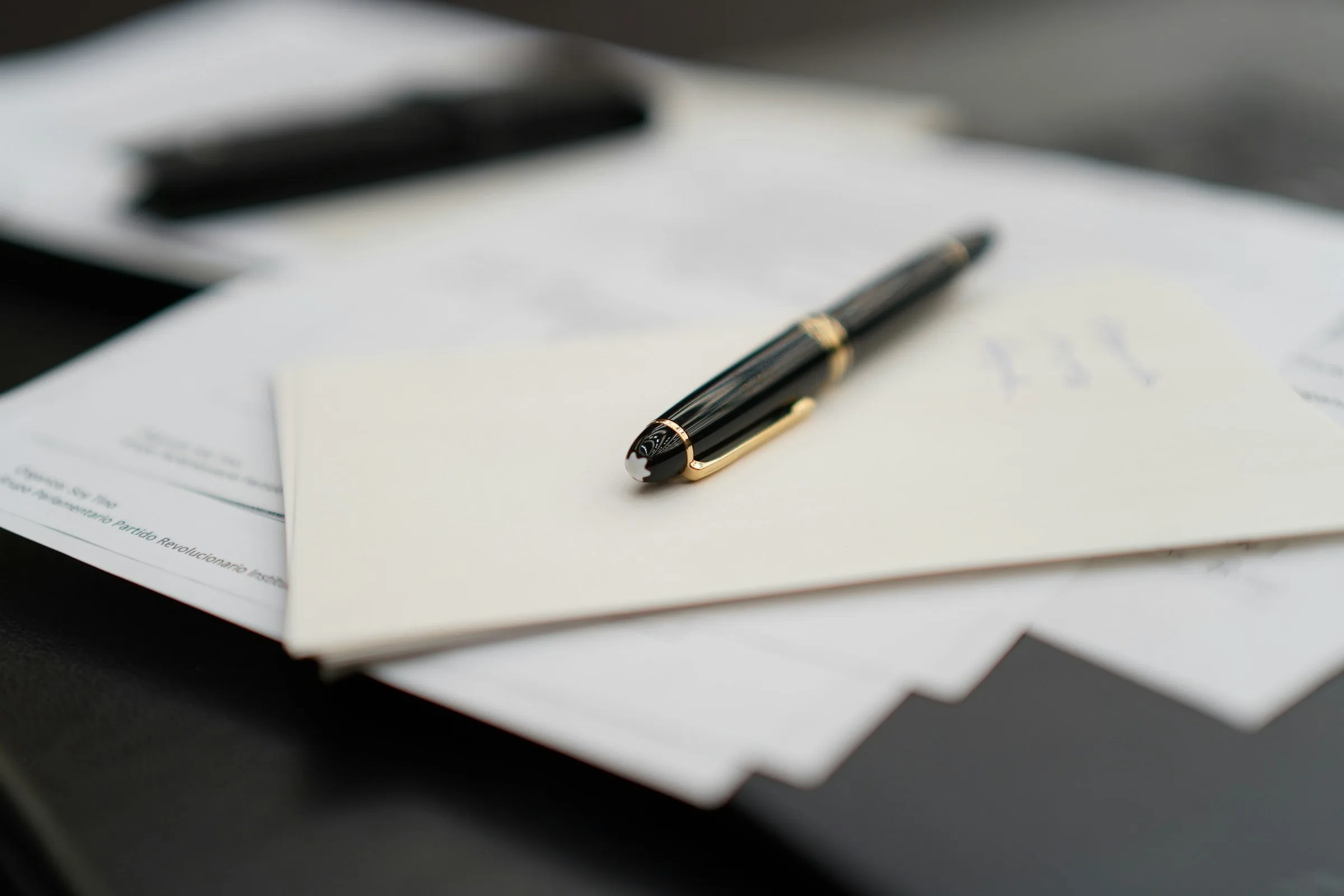 A fountain pen resting on a sheet of paper and an envelope on a desk, with more papers behind