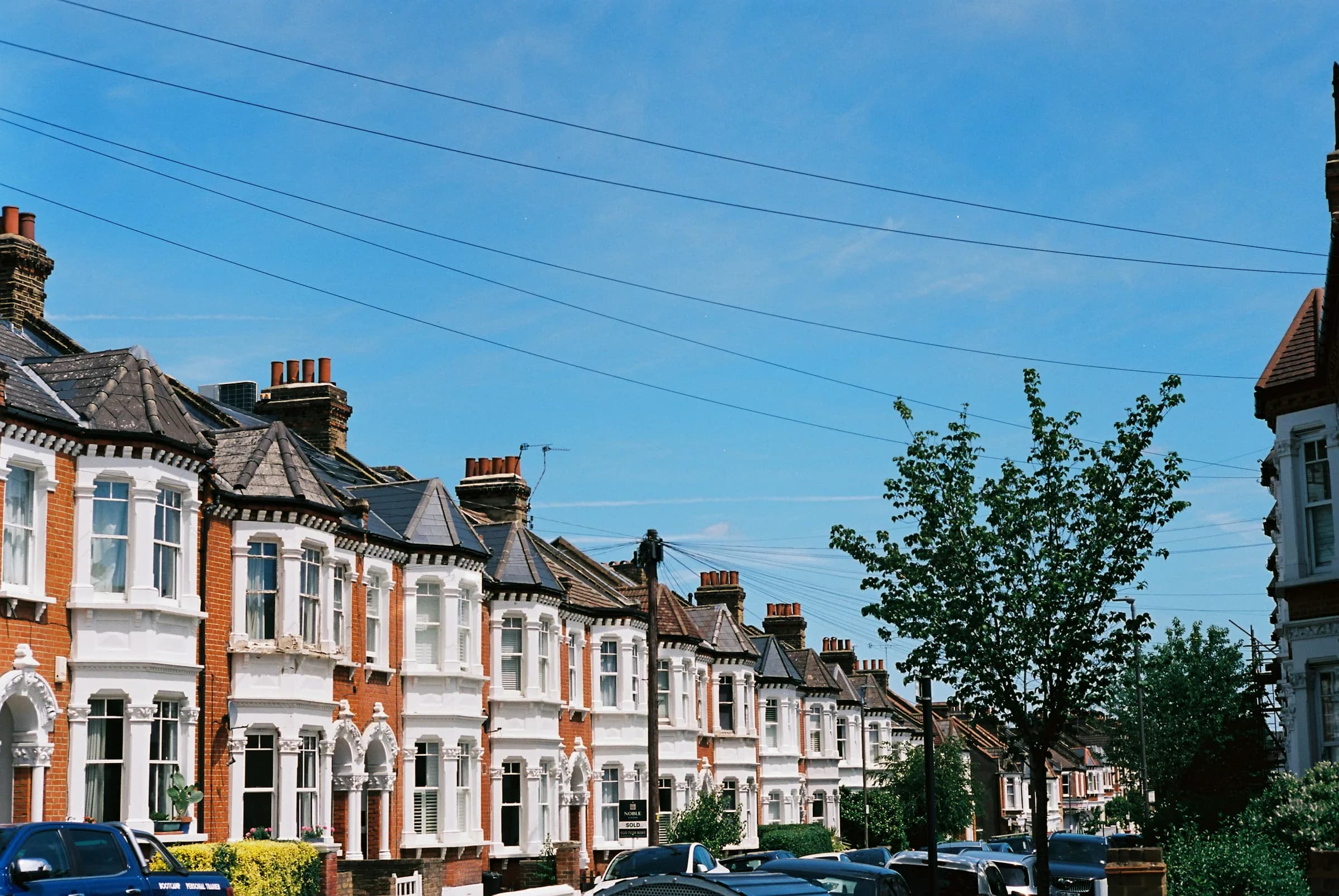 A row of Edwardian terraced houses with bay windows and brick frontages under a clear blue sky