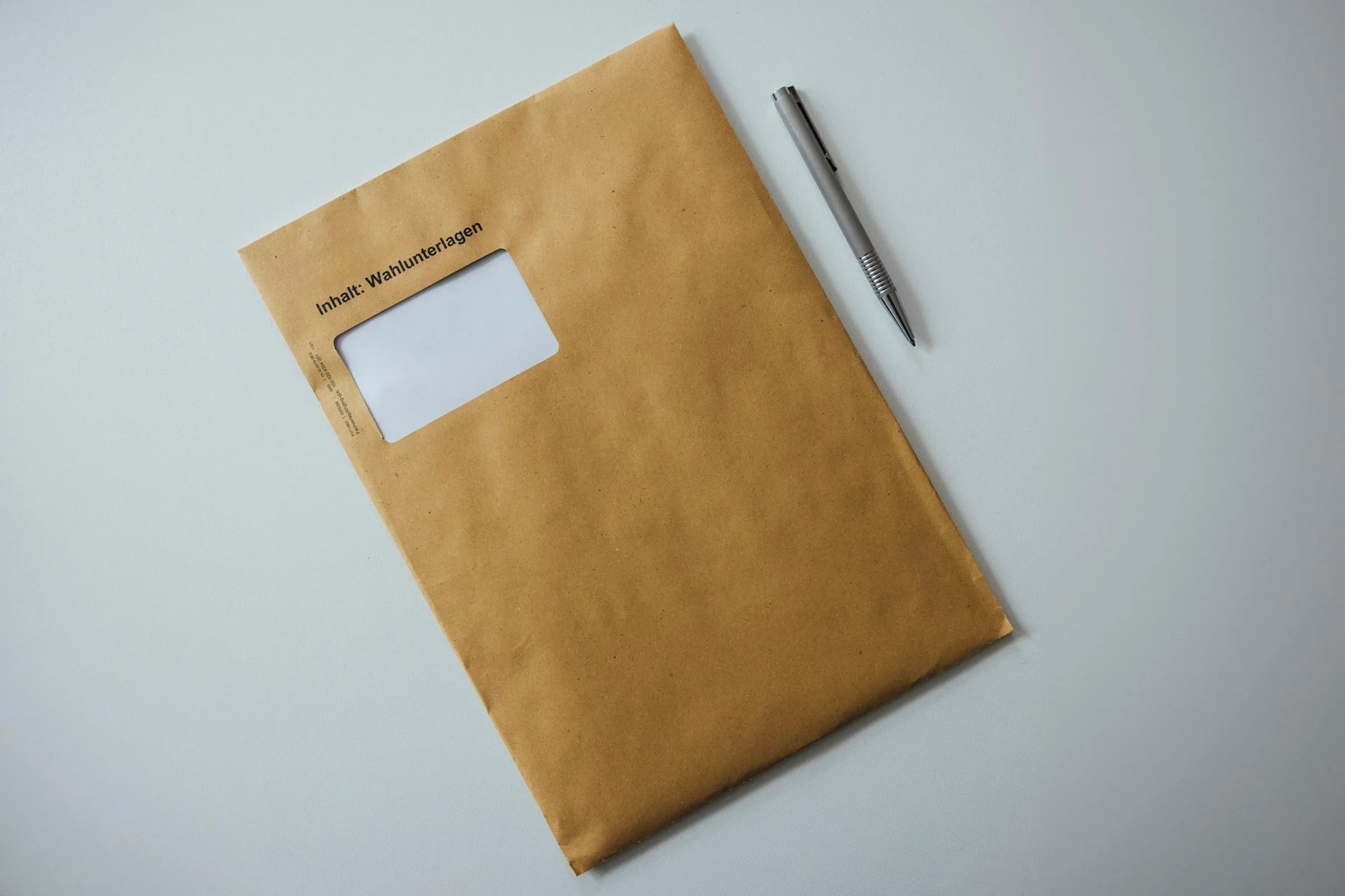 A brown paper window envelope and a pen lying on a pale blue-grey surface.