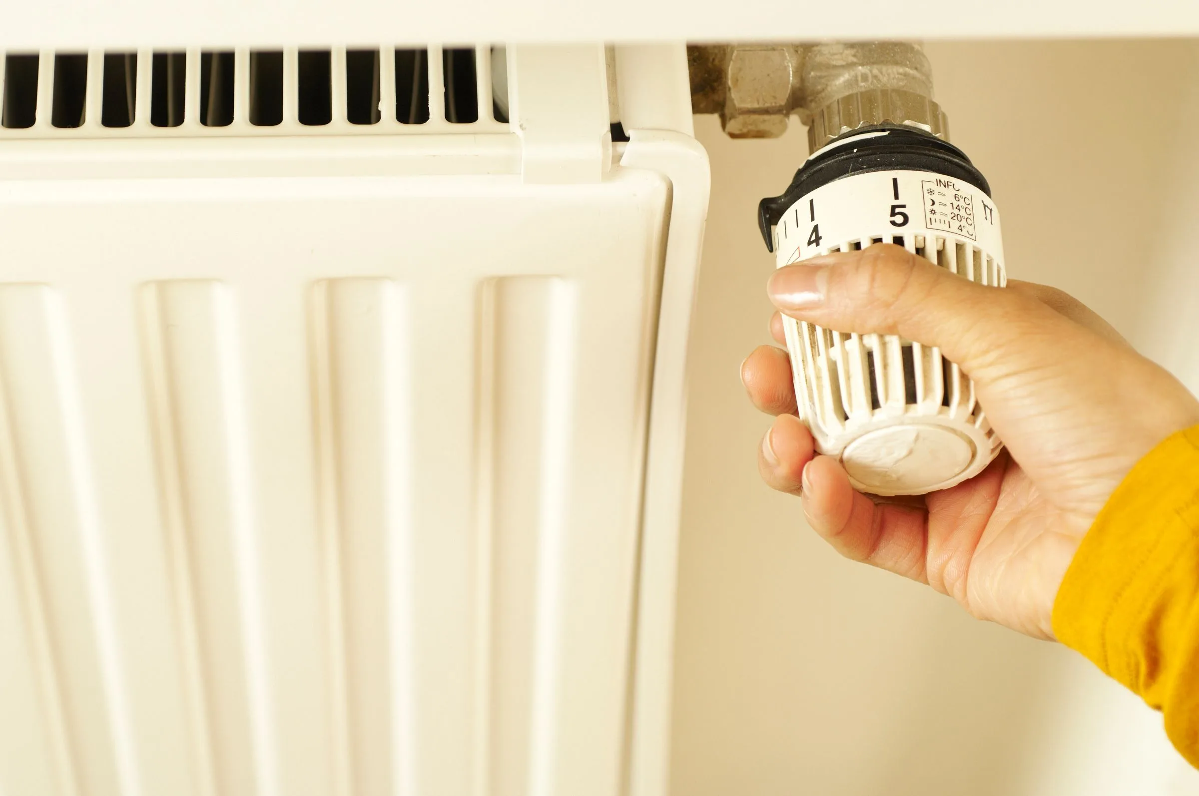 A hand turning the white thermostatic valve on a white panel radiator.