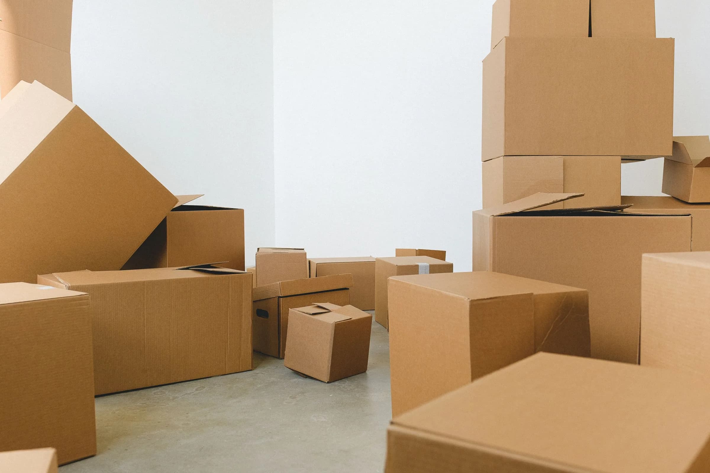 Cardboard moving boxes stacked and scattered across the floor of a bright, empty room.