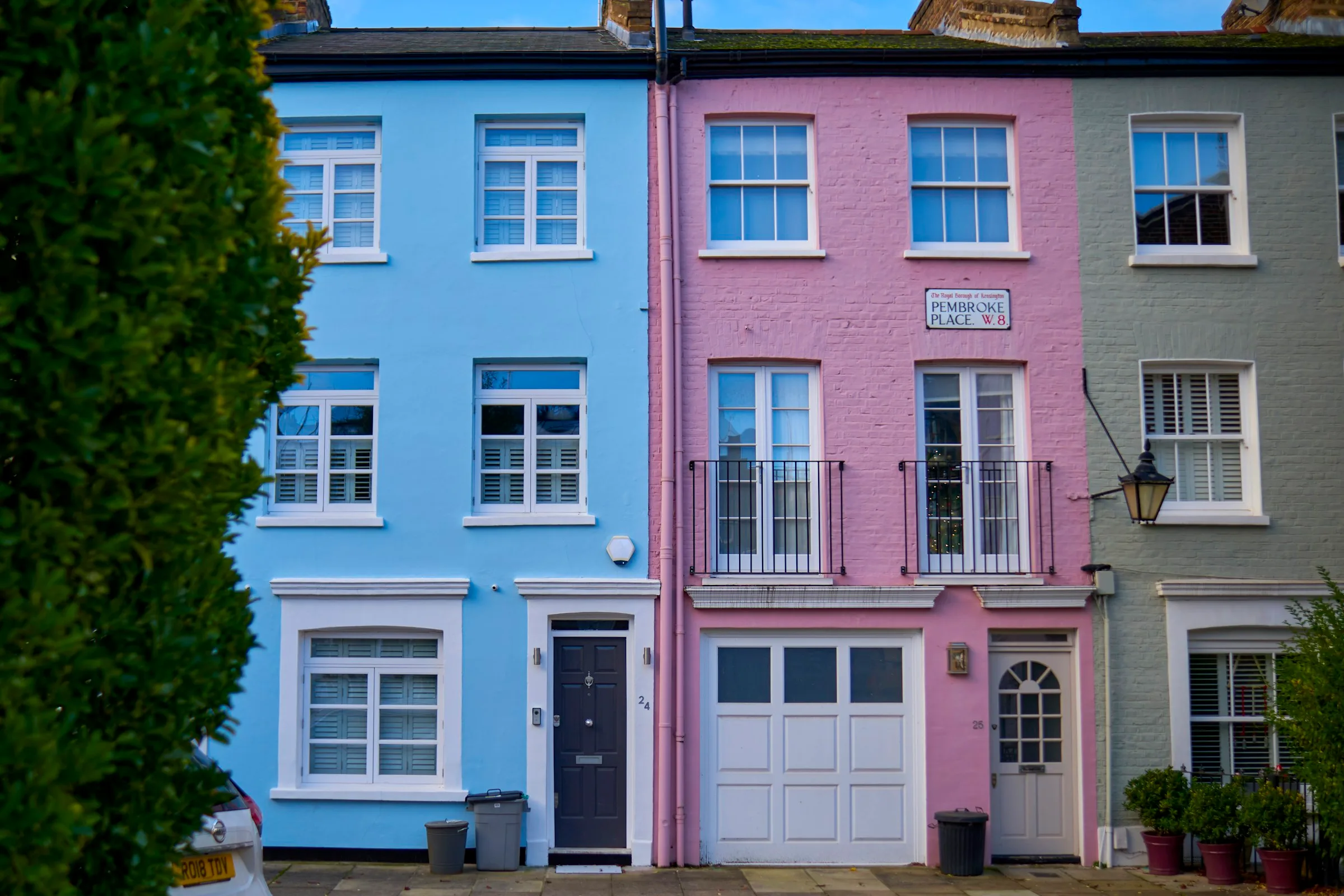 A terrace of tall houses painted pale blue, pink and grey on a quiet street