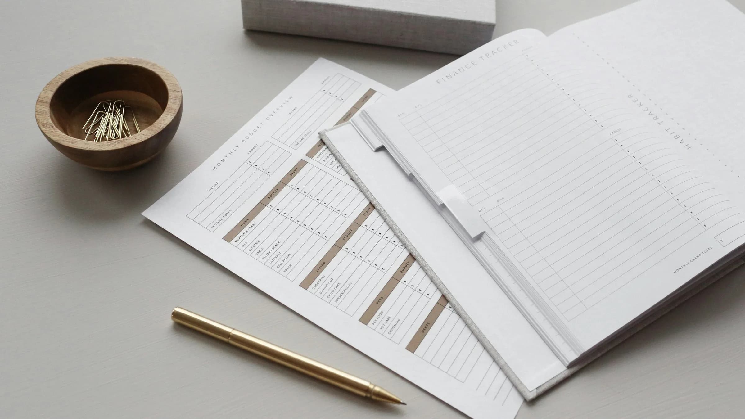 Printed forms in a folder on a grey desk beside a gold pen and a small bowl of paper clips