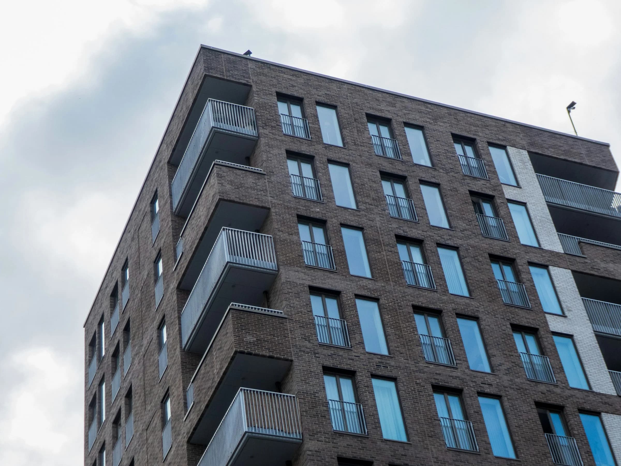 A modern brick apartment block with balconies, seen from below against a cloudy sky