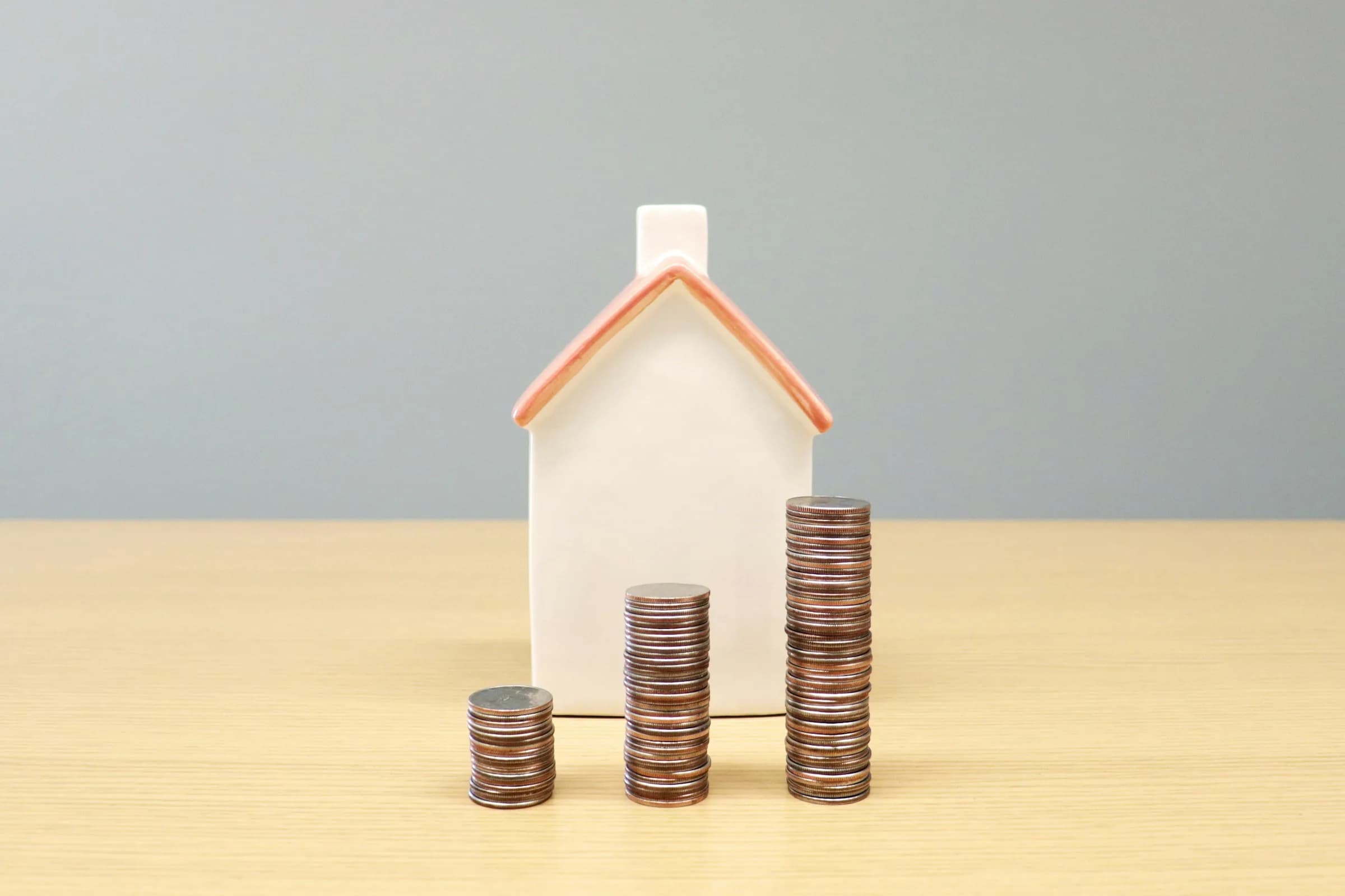 A small white model house with an orange roof beside stacks of coins in rising heights