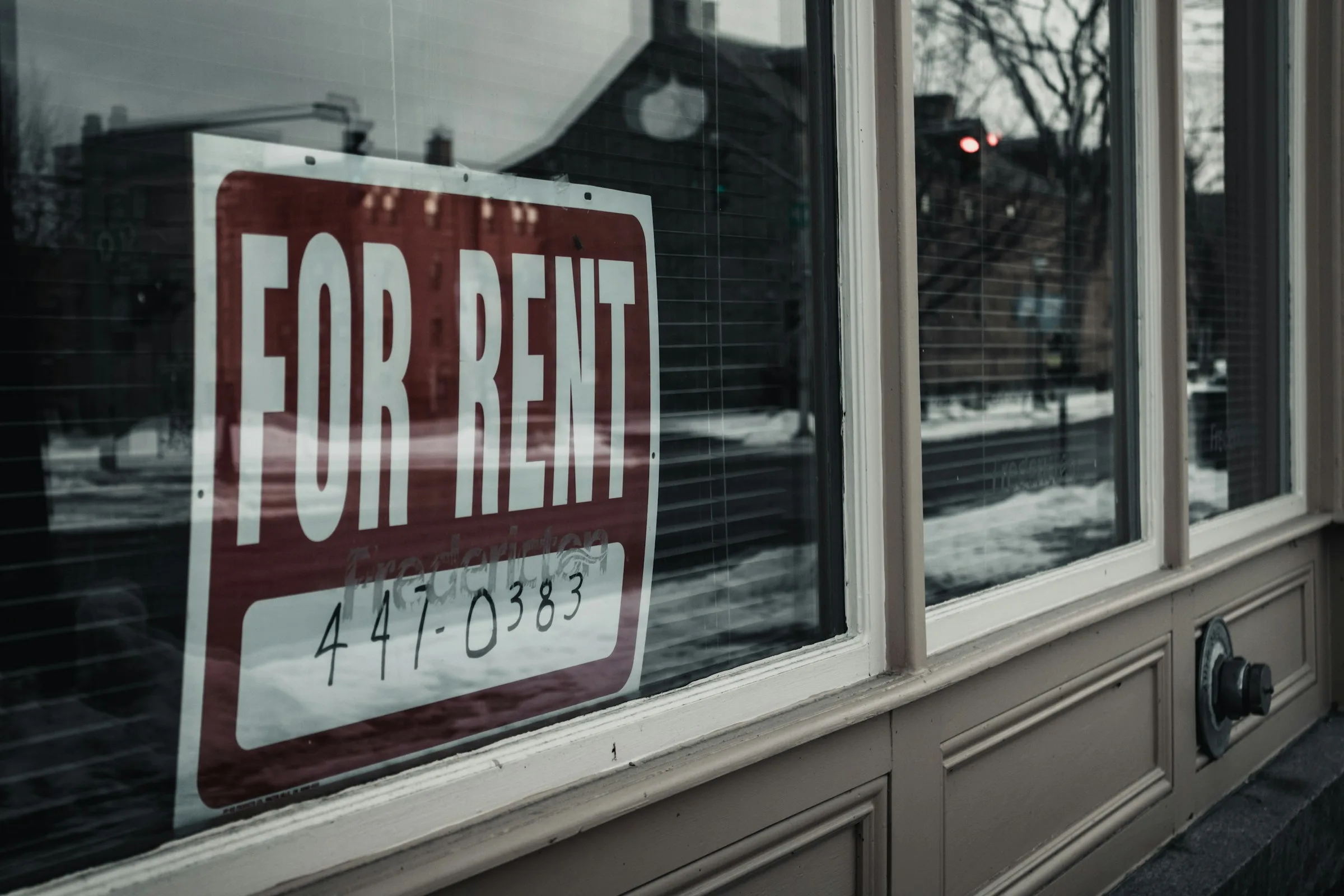 A red and white “For Rent” sign hanging in a shop window