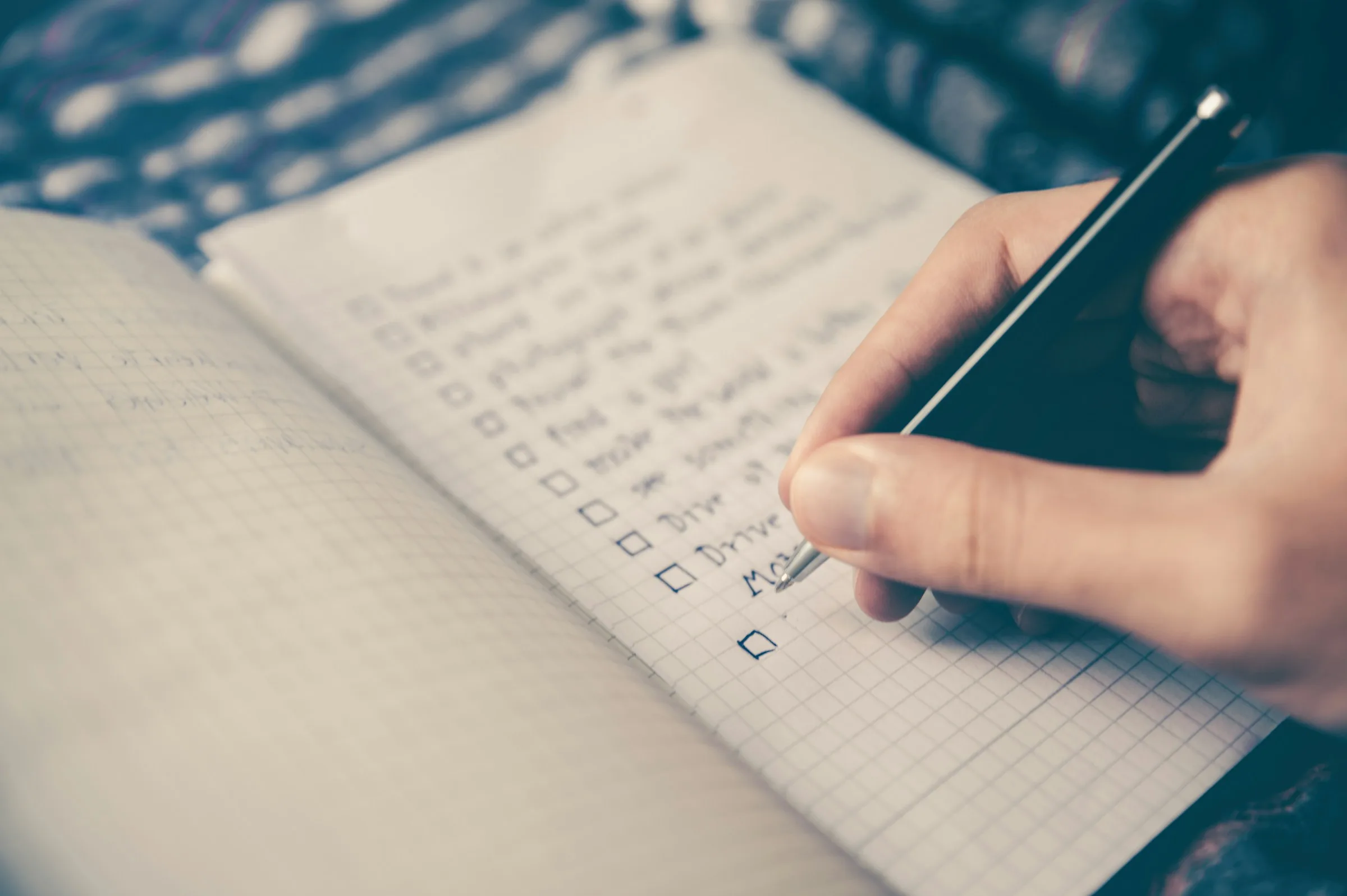 A person writing a list of ticked items in a notebook with a pen